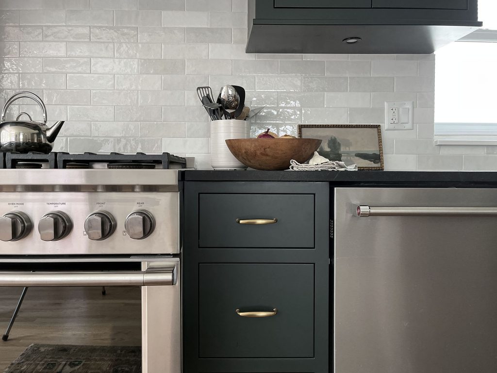 Detail shows the brass drawer pulls on the inset drawers as well as a small paiting, a wooden bowl and a utensil holder.